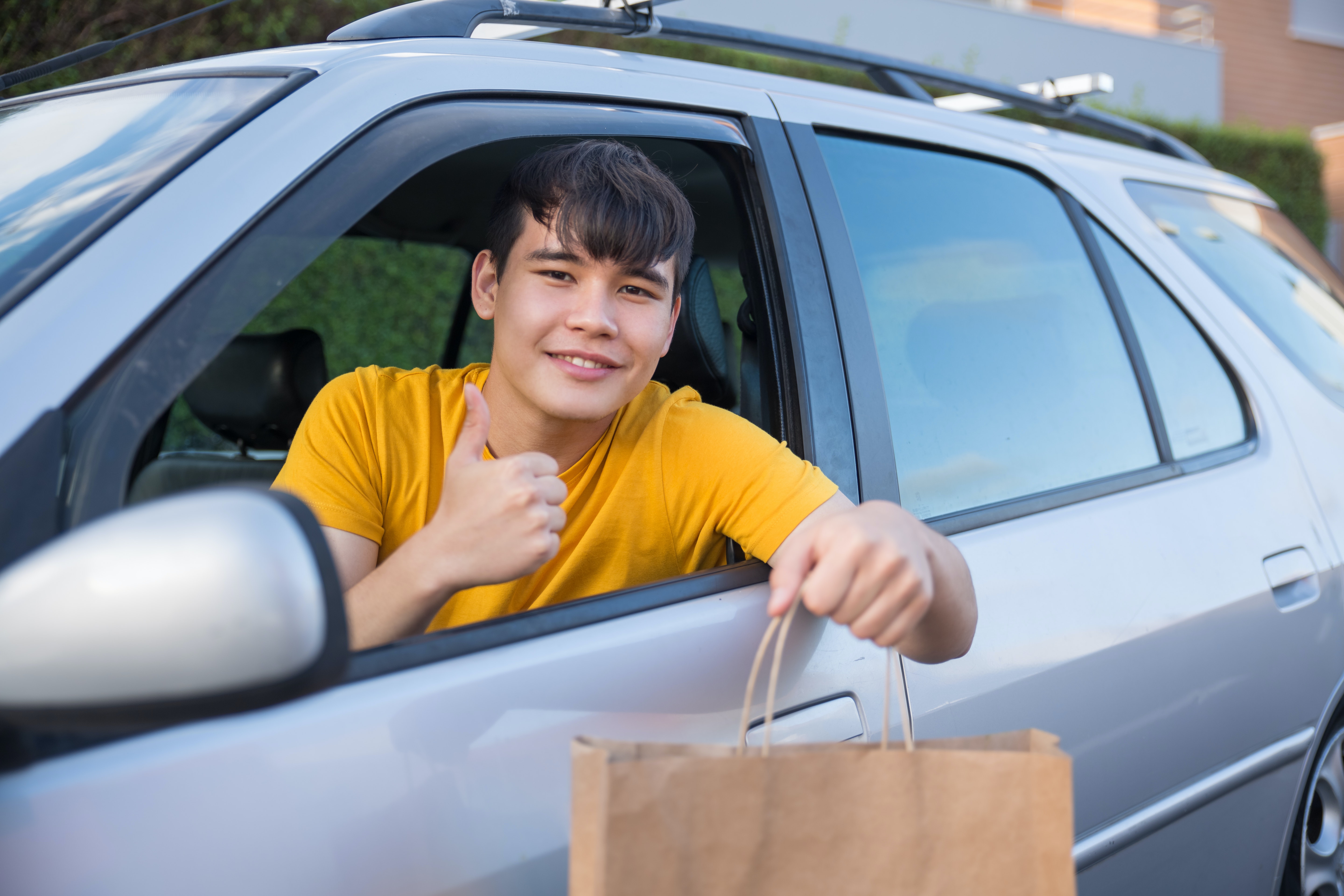 A driver holding a paper bag out of their car window.