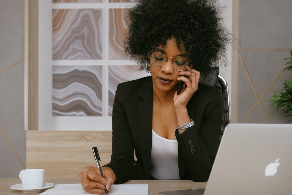 A woman talking on the phone while writing something down.