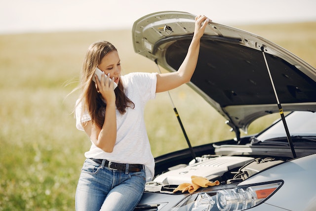 Una mujer revisa el motor de su coche. Está hablando por teléfono.