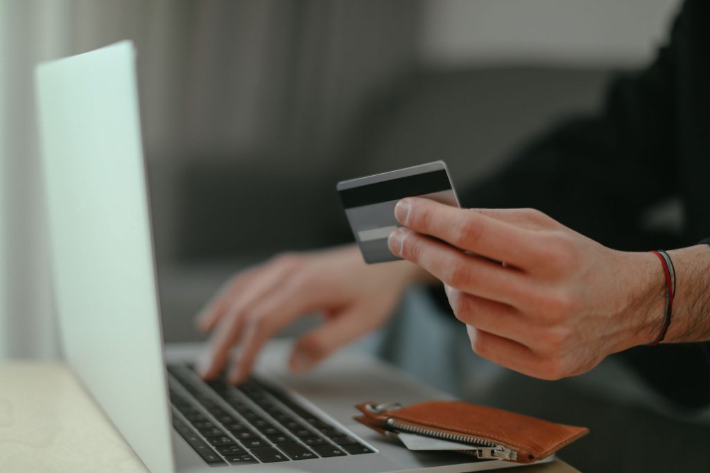 Someone holds a credit card in one hand while typing on their laptop.